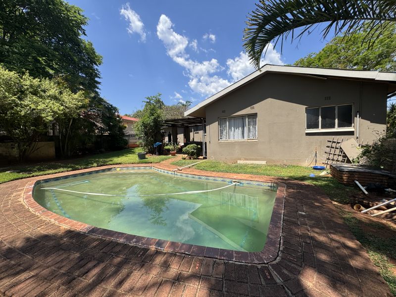 Rear garden area featuring a swimming pool with brick paving and a covered patio attached to the main house structure.