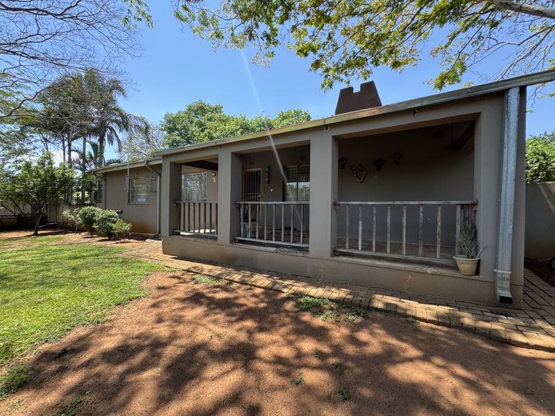Rear view of the house featuring a covered patio area with a brick-paved walkway and a large garden space.