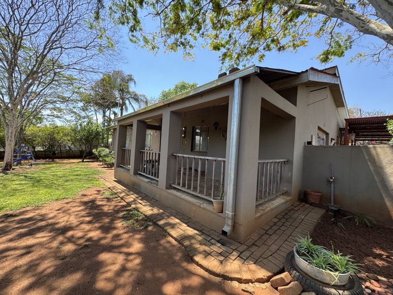 A view of the rear exterior featuring a covered patio with concrete pillars, timber railings, and brick paved pathways leading into the garden.