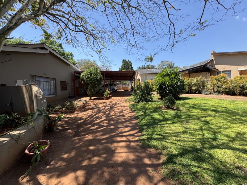 A spacious rear garden featuring a large lawn, established trees, and a covered carport area providing convenient off-street parking.
