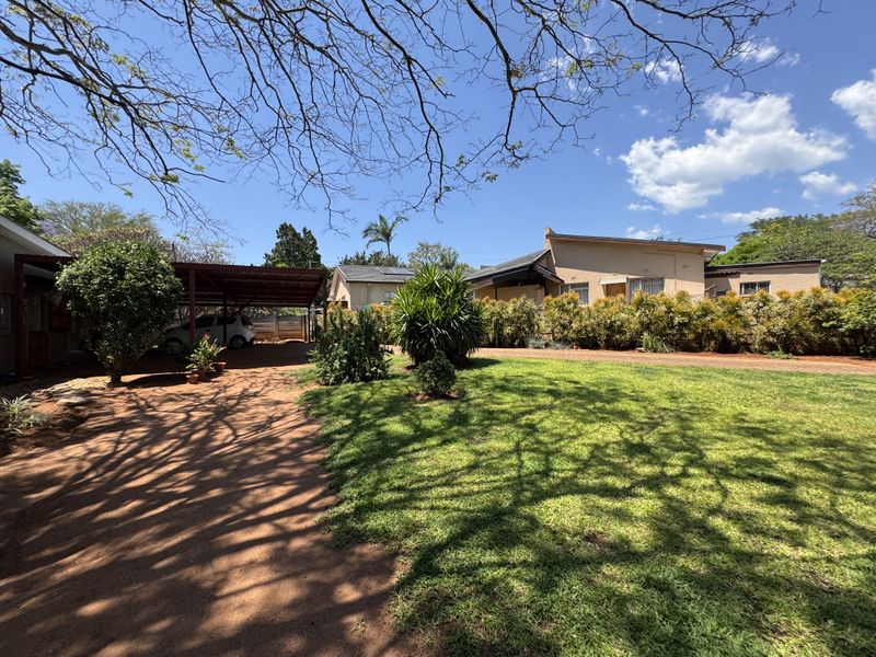 Front view of the property featuring a spacious garden, paved driveway, and a covered carport area.