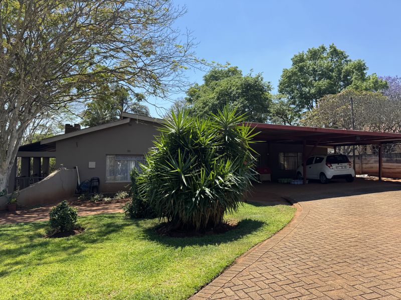 Front view of the property featuring a paved driveway, a spacious carport, and a well-maintained garden area.