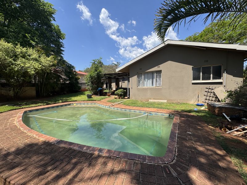 Rear garden area featuring a swimming pool with brick surround, lawn, and exterior building facade.