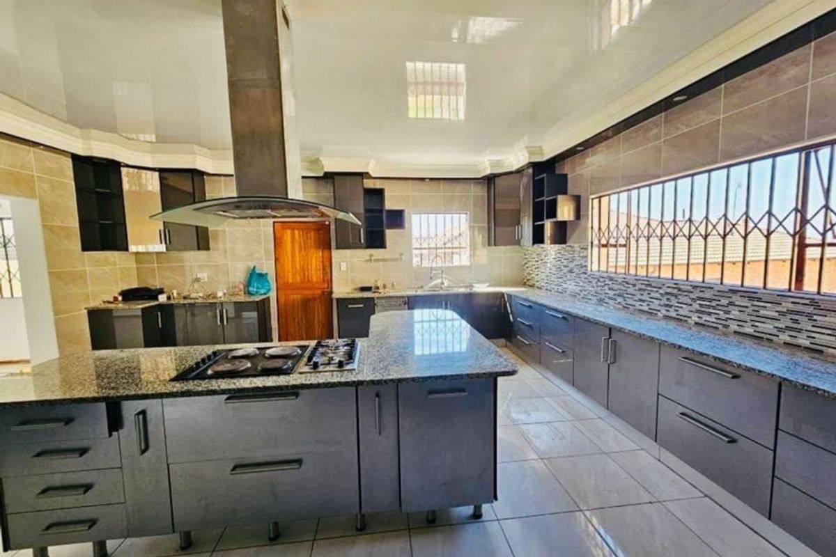Modern kitchen featuring extensive dark cabinetry, granite countertops, a central island with a built-in gas hob, and tiled finishes throughout.