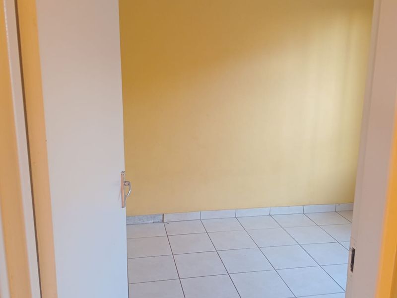 An empty bedroom featuring yellow walls and tiled flooring with some visible damage to the tiles.