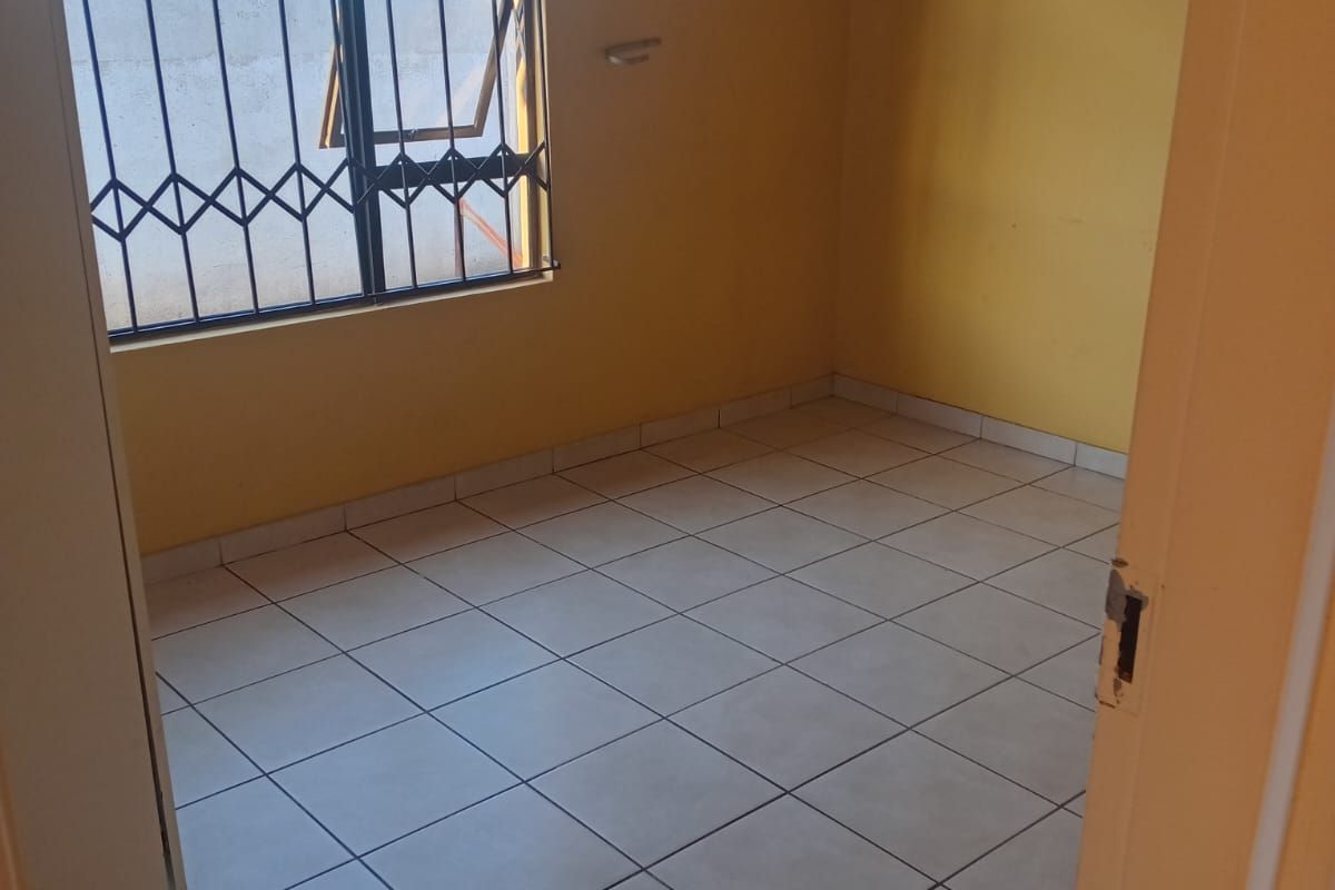 An empty bedroom featuring tiled flooring and a window with a security gate, offering a blank canvas for potential renovation or styling.
