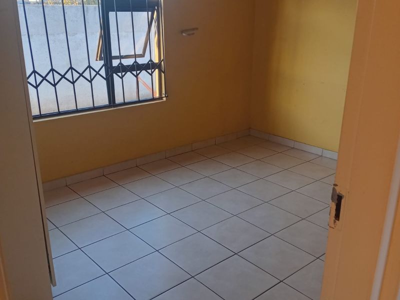 An empty bedroom featuring tiled flooring and a window with a security gate, offering a blank canvas for potential renovation or styling.