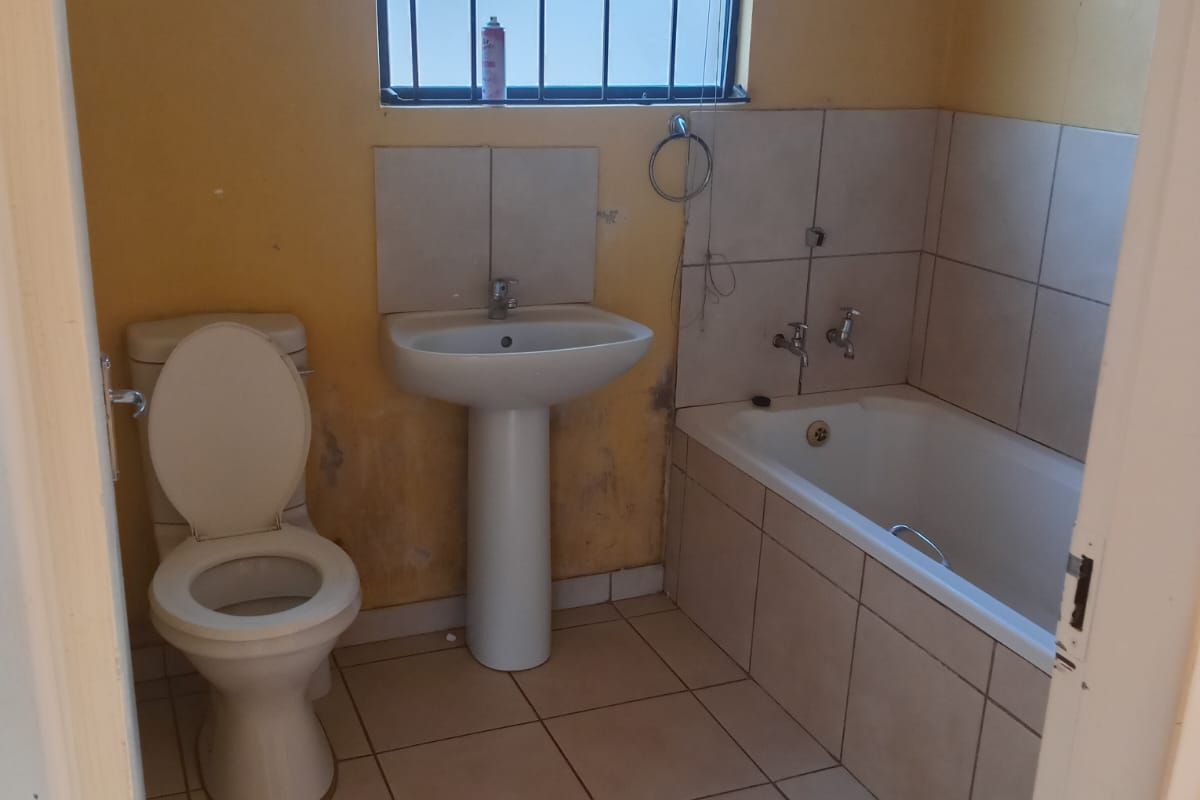 A functional bathroom featuring a pedestal basin, toilet, and built-in bathtub, requiring cosmetic updates to the wall finishes.
