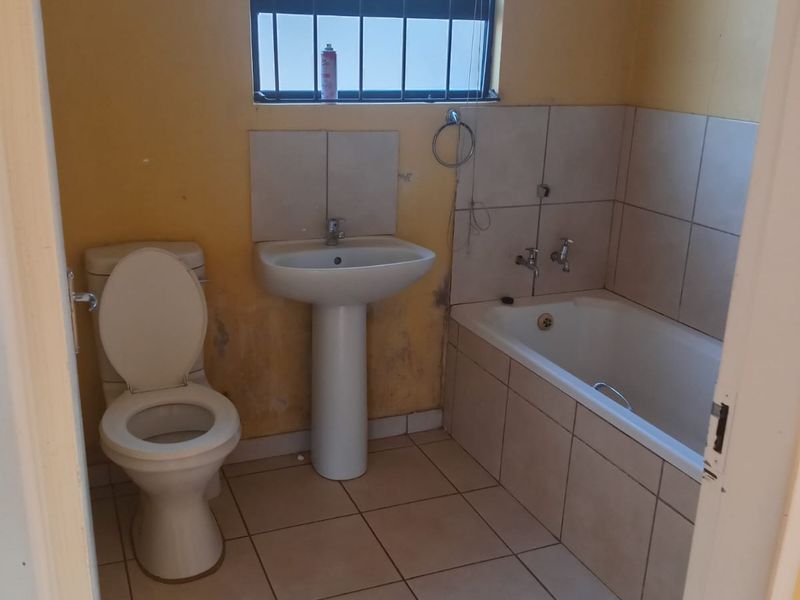 A functional bathroom featuring a pedestal basin, toilet, and built-in bathtub, requiring cosmetic updates to the wall finishes.