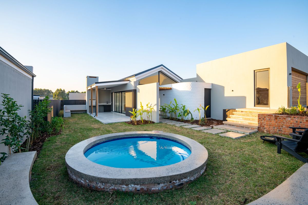 A modern rear garden featuring a circular plunge pool, a covered patio with a built-in braai, and well-maintained landscaping with concrete steps.