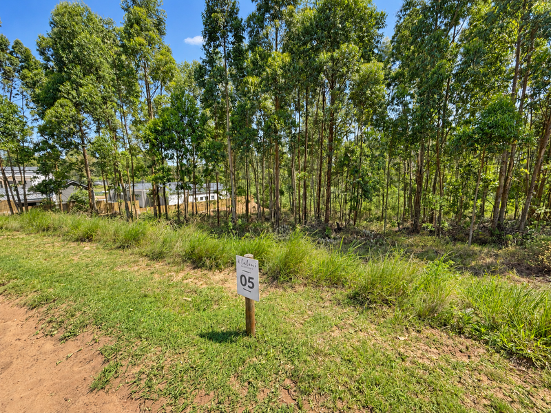 A vacant residential plot featuring established trees and natural vegetation, marked with a property identification sign.