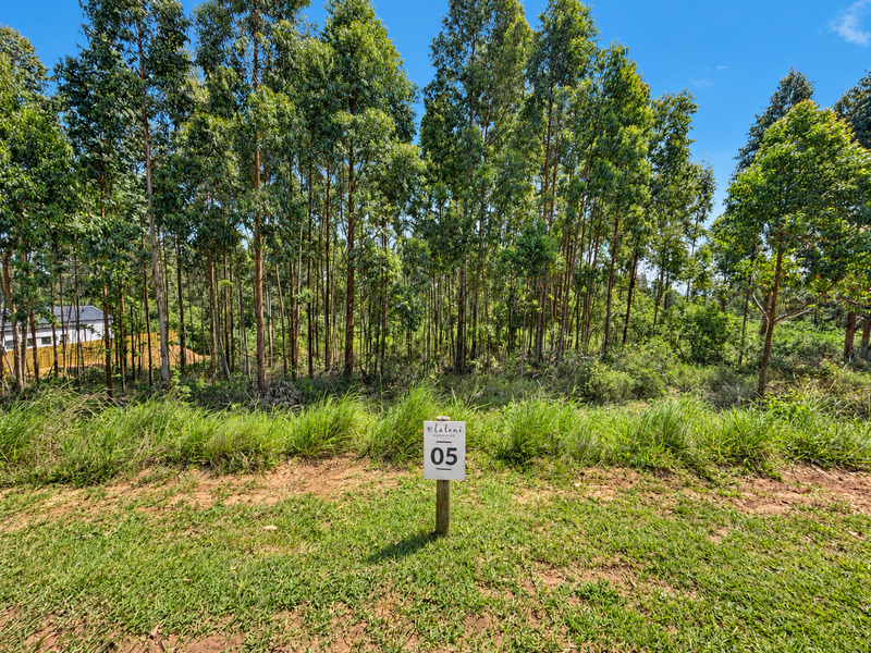 A view of a vacant residential plot featuring established trees and natural grass coverage, marked with a property identification sign.