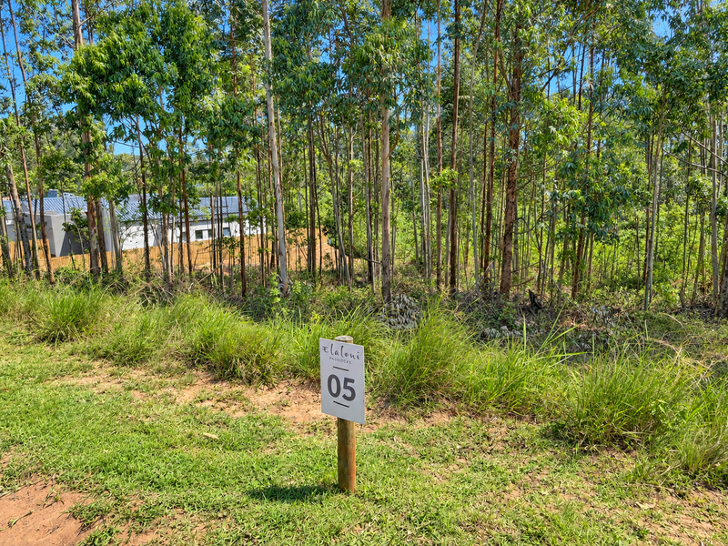 A view of a vacant residential plot featuring established eucalyptus trees and a property marker, situated within a residential estate.