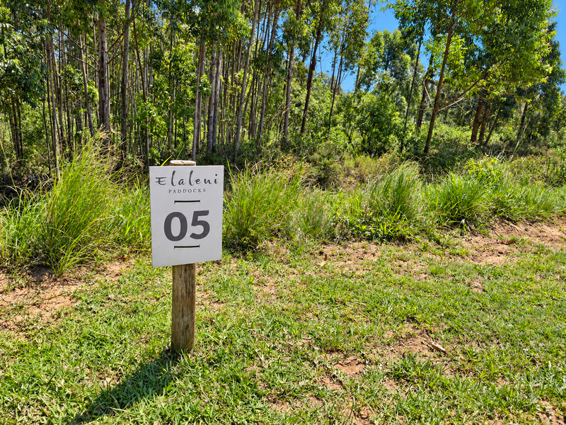 A view of a vacant residential plot featuring natural vegetation and a property identification sign.