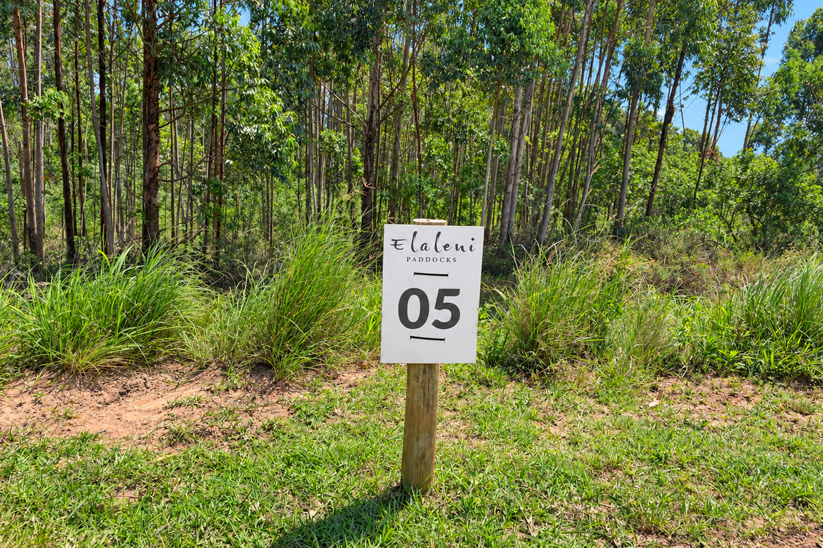 A vacant residential plot marked with a property identification sign, featuring natural vegetation and mature trees in a peaceful setting.