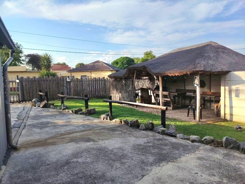 A rear garden area featuring a thatched roof patio, paved outdoor space, and timber fencing, providing a rustic outdoor entertainment setting.