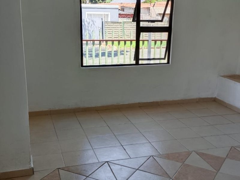 An empty living room featuring tiled flooring and a window with an aluminium frame, offering a blank canvas for interior design.