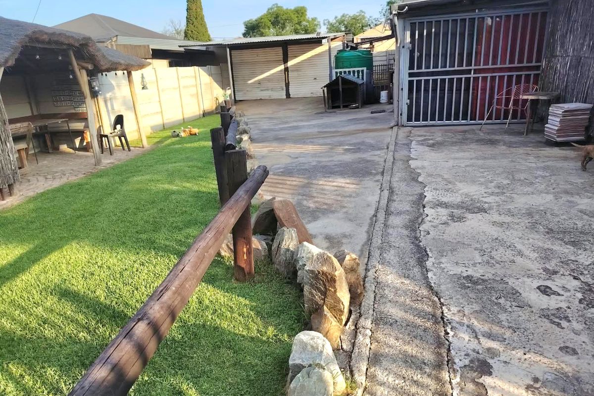 Rear yard featuring a thatched lapa, concrete driveway, perimeter walling, and a garage with a metal security gate.