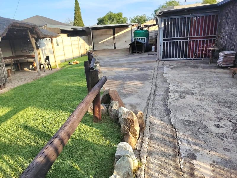 Rear yard featuring a thatched lapa, concrete driveway, perimeter walling, and a garage with a metal security gate.