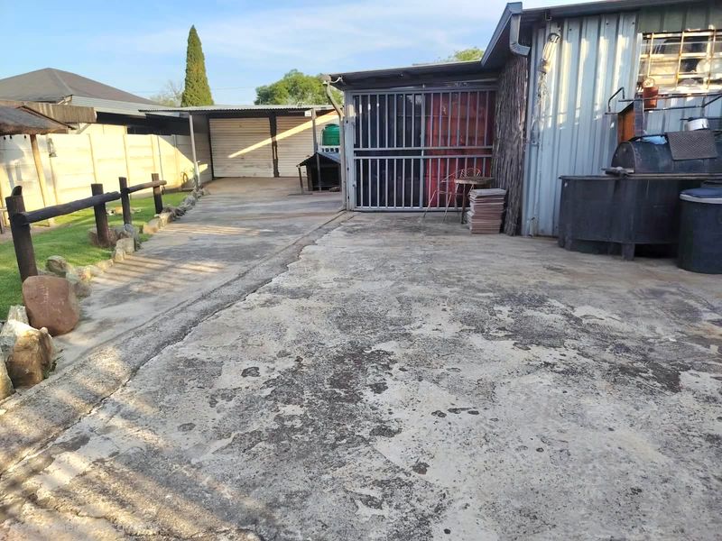 Rear exterior area featuring a concrete driveway, metal garage structure, and perimeter precast concrete walling.