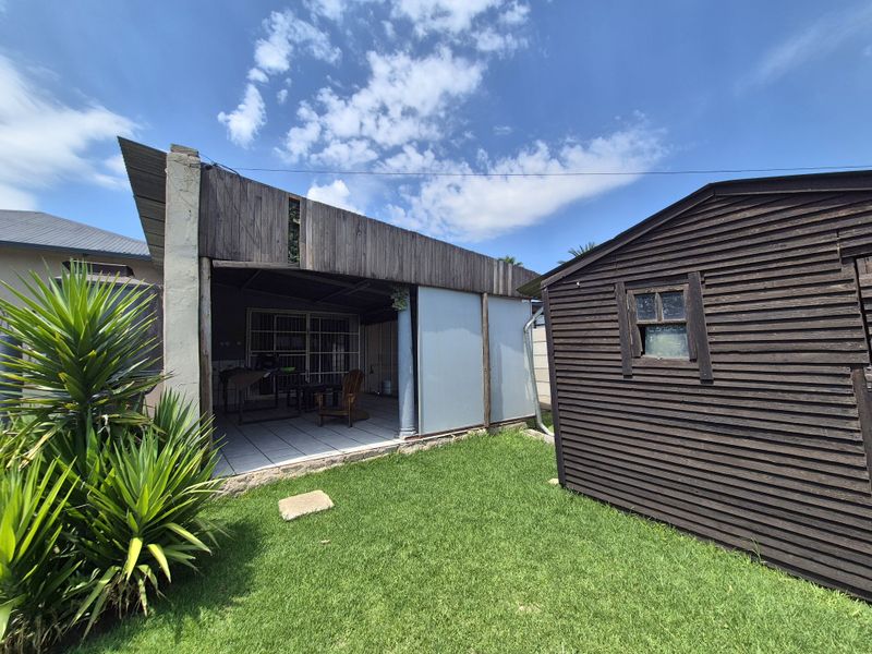 Rear garden view featuring a covered patio area with tiled flooring and an adjacent timber storage shed set within a grassed yard.