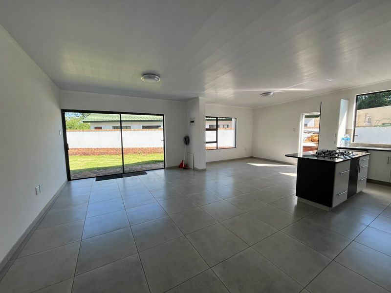 Spacious open-plan living and kitchen area featuring large format floor tiles, a modern kitchen island with a gas hob, and sliding doors to the garden.