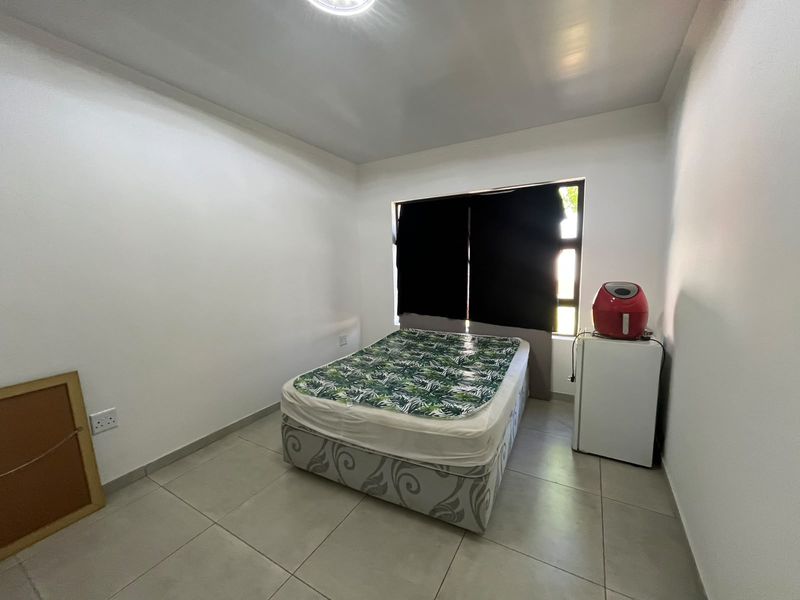 A simple bedroom featuring neutral tiled flooring, white walls, and a window with dark curtains, providing a clean and functional living space.