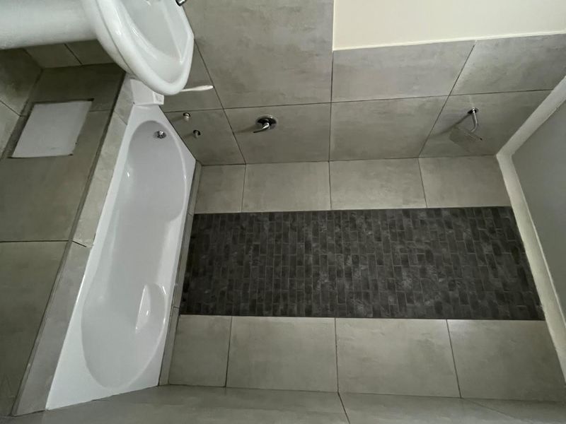 A compact bathroom featuring a pedestal basin, built-in bathtub, and modern grey tiled finishes throughout.