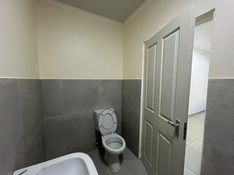 A clean, functional bathroom featuring neutral wall paint, grey ceramic wall tiles, and tiled flooring.