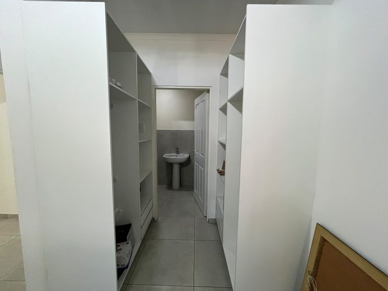 A walk-through dressing area featuring extensive built-in cabinetry, leading into an en-suite bathroom with a pedestal basin and neutral floor tiling.