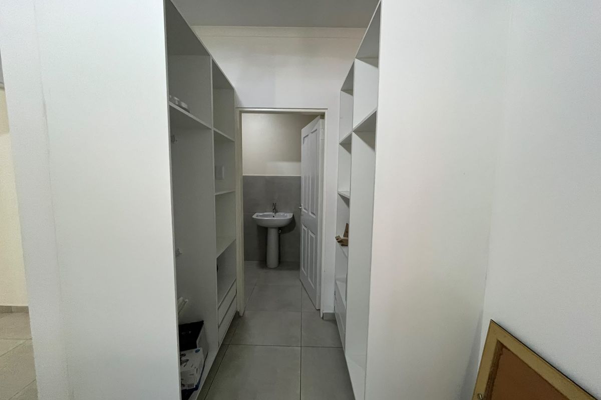 A walk-through dressing area featuring extensive built-in cabinetry, leading into an en-suite bathroom with a pedestal basin and neutral floor tiling.
