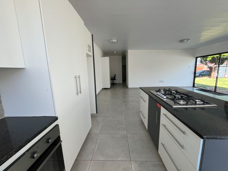 Modern kitchen featuring a central island with a gas hob, granite countertops, built-in oven, and sleek white cabinetry with tiled flooring.