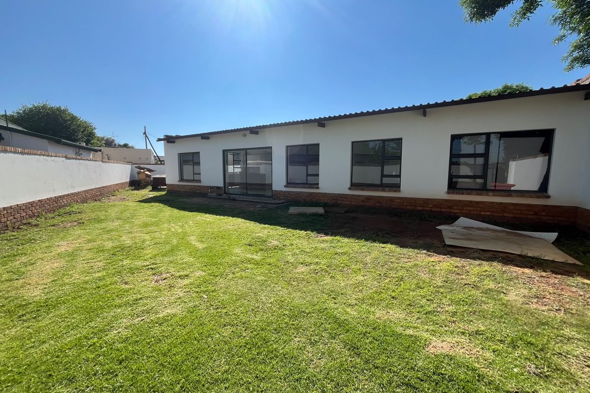 Rear view of the property featuring a spacious lawn, brick boundary wall, and multiple aluminium-framed windows and sliding doors.