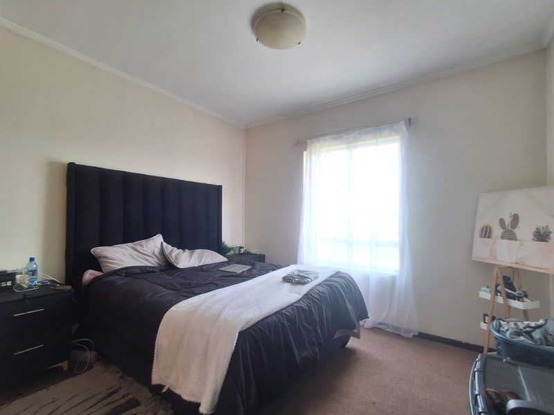 A standard bedroom featuring neutral walls, carpeted flooring, and a window with a curtain rod, providing a functional and well-lit living space.