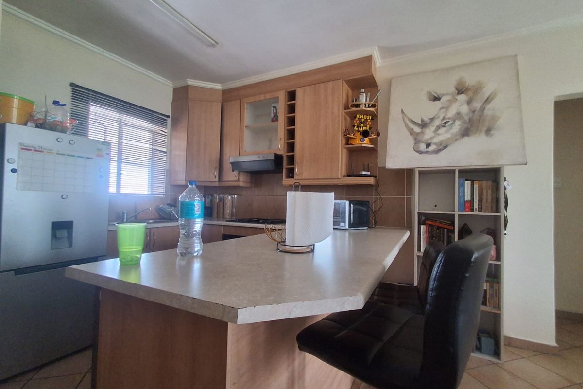 A functional kitchen featuring light wood-finish cabinetry, a central island with breakfast bar seating, and tiled flooring.