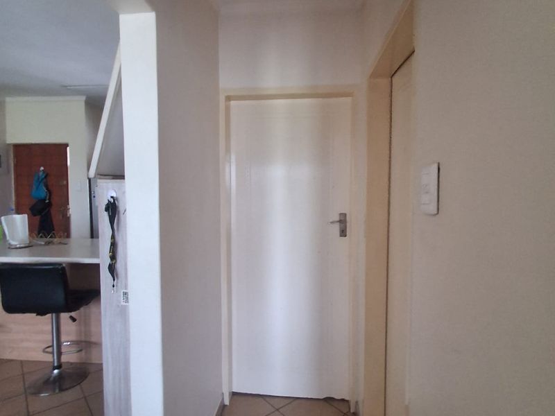 A functional hallway featuring tiled flooring and access to adjacent rooms, with a view into the open plan living area.