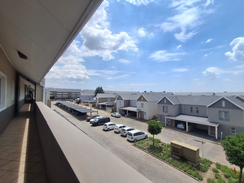 A covered balcony walkway overlooking the residential complex parking area and surrounding townhouse units.
