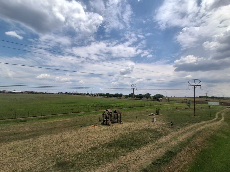 An elevated view overlooking an open field with a playground area and overhead power lines under a cloudy sky.