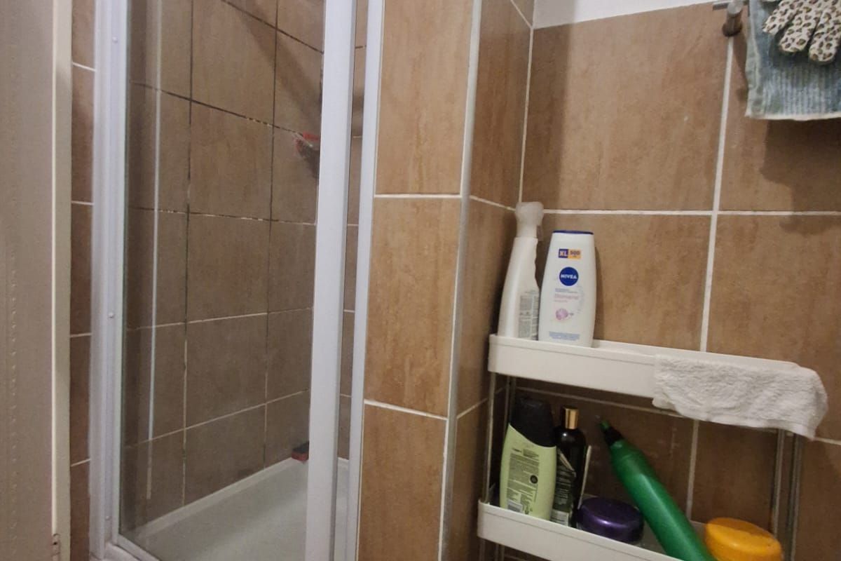 A functional bathroom featuring a shower enclosure with tiled walls and flooring, including a wall-mounted towel rail.