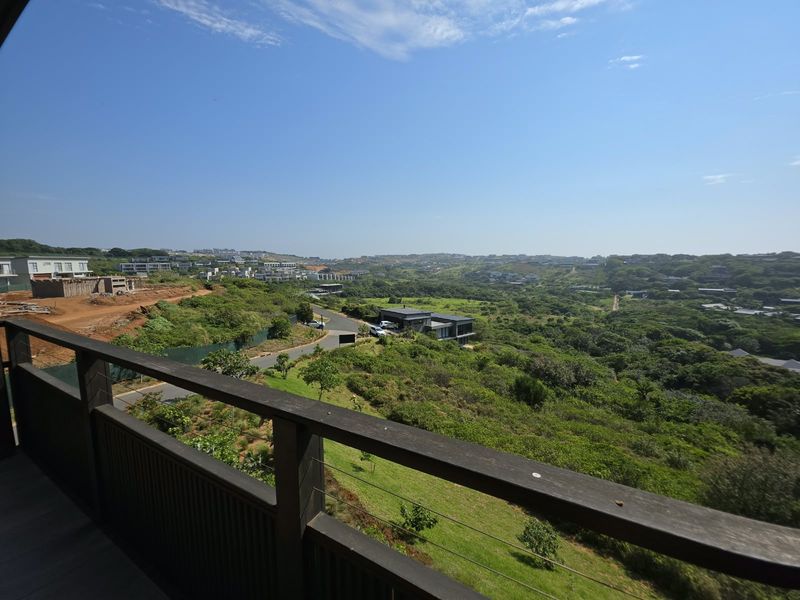 Elevated panoramic view overlooking a lush green landscape and residential estate, captured from a timber-railed balcony.