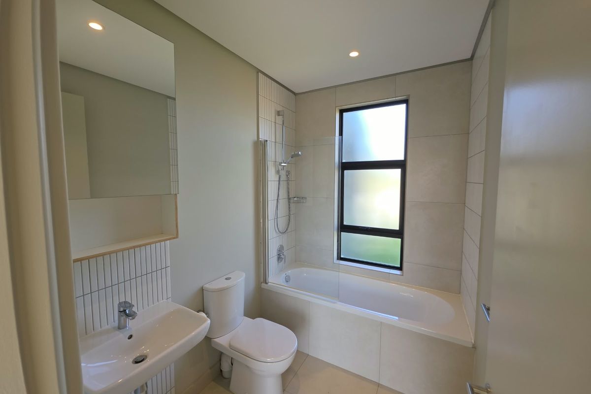 A modern, clean bathroom featuring a built-in bathtub with a glass screen, a wall-mounted basin, and neutral tiling throughout.