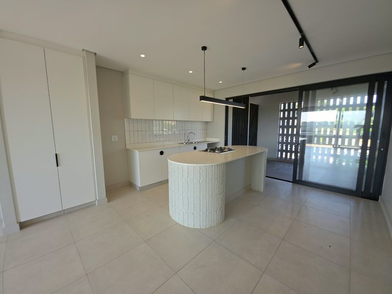 Modern kitchen featuring a curved island with a gas hob, sleek white cabinetry, tiled backsplash, and seamless access to an outdoor patio area.