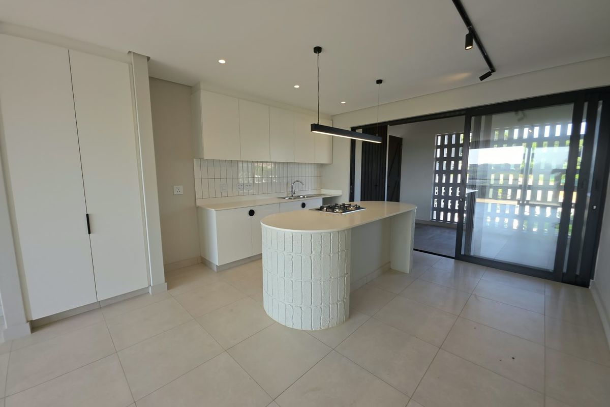 Modern kitchen featuring a curved island with a gas hob, sleek white cabinetry, tiled backsplash, and seamless access to an outdoor patio area.