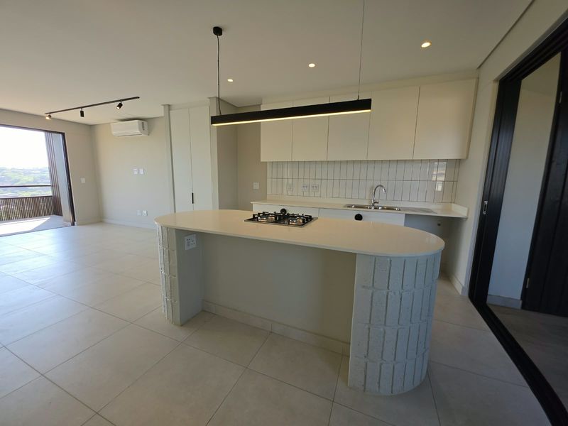 Modern open-plan kitchen and living area featuring a curved island with a gas hob, sleek cabinetry, tiled flooring, and access to a private balcony.