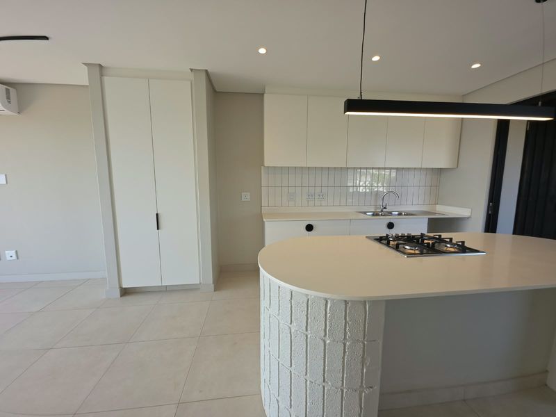 Modern kitchen featuring sleek white cabinetry, stone countertops, a central island with a gas hob, and contemporary tiled finishes.