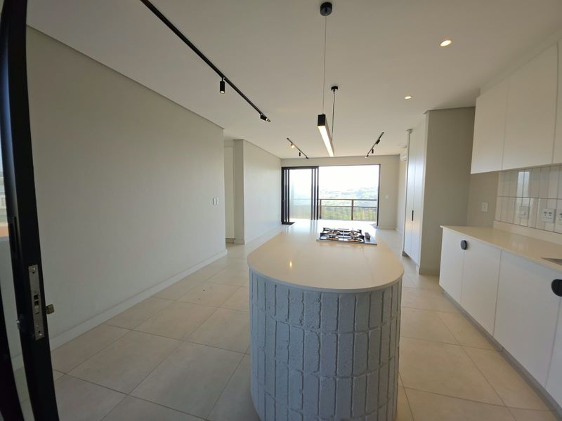 Modern open-plan kitchen and living area featuring a central island with a gas hob, sleek cabinetry, and large sliding doors leading to a balcony.