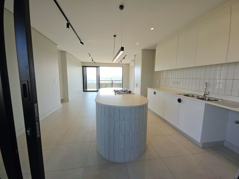 Modern open-plan kitchen and living area featuring a unique curved island, sleek white cabinetry, gas hob, and large sliding doors leading to a balcony.