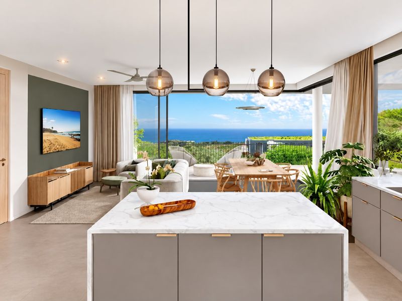 Modern open-plan living and kitchen area featuring a marble-topped island, contemporary pendant lighting, and expansive sliding doors opening to a scenic ocean view balcony.