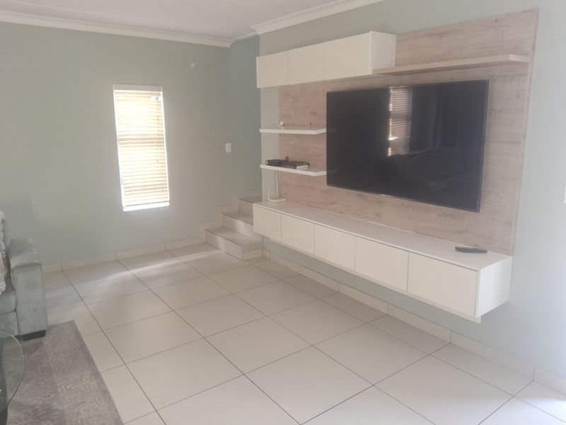 A modern living room featuring a sleek, wall-mounted built-in media unit, light-colored tiled flooring, and neutral wall tones with natural light from a window.
