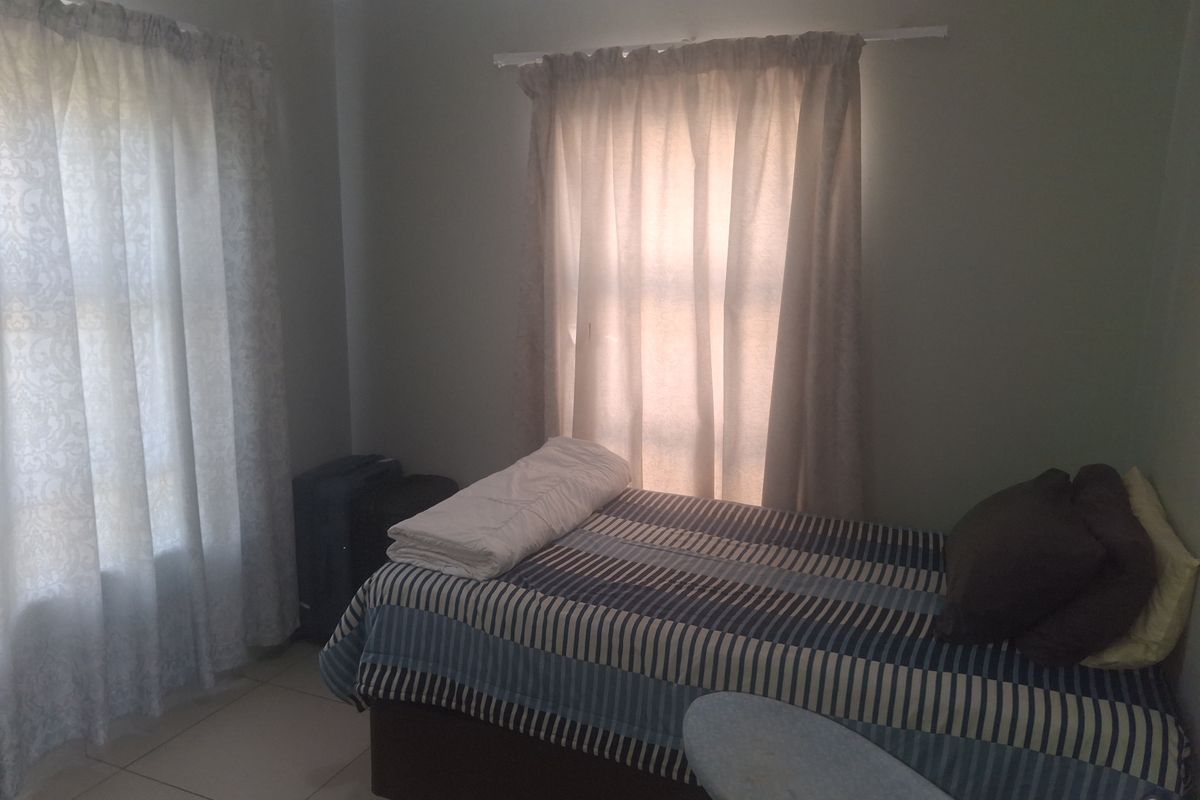 A functional bedroom featuring tiled flooring and dual windows with installed curtain rails, providing natural light to the space.